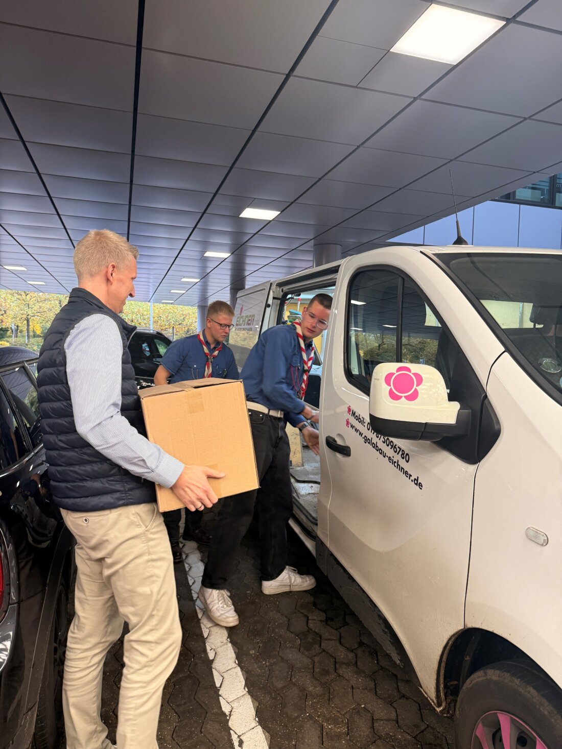 Foto: Thomas Franken (Messe Düsseldorf) übergibt Mehrwegbecher und hilft beim Verladen für die Lieferung an die örtliche Pfadfindergruppe, um die Kreislaufwirtschaft für Kunststoffe und das Engagement in der Gemeinde zu fördern.